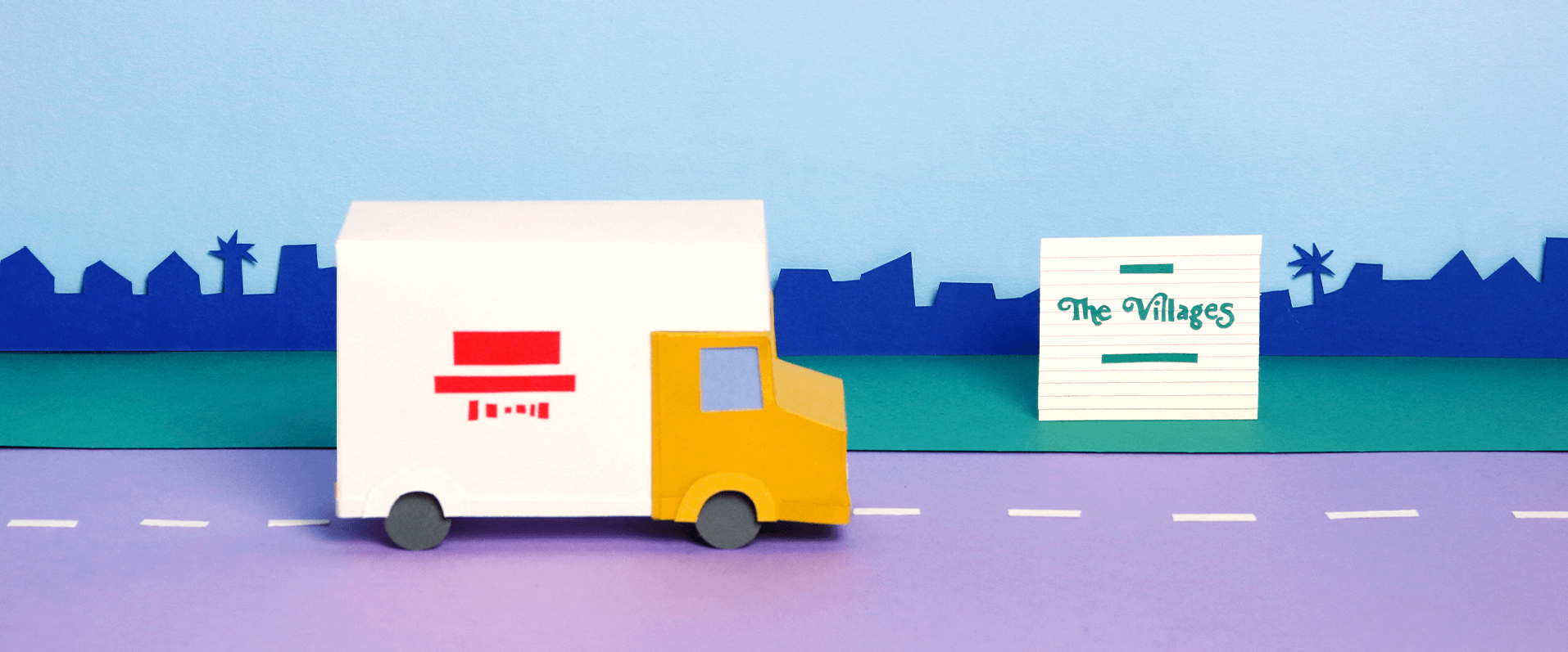 Paper cut out of moving truck passing by a sign that says 'The Villages'
